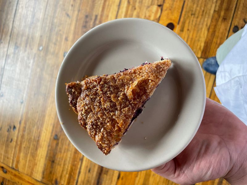 A hand holding a plate with a slice of blueberry pie