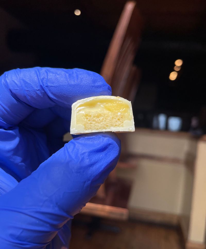 A gloved hand holding a Meyer lemon bonbon cut to show its yellow filling