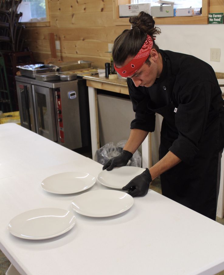 A younger Anthony in a red bandana, focused, setting out plates for a private service
